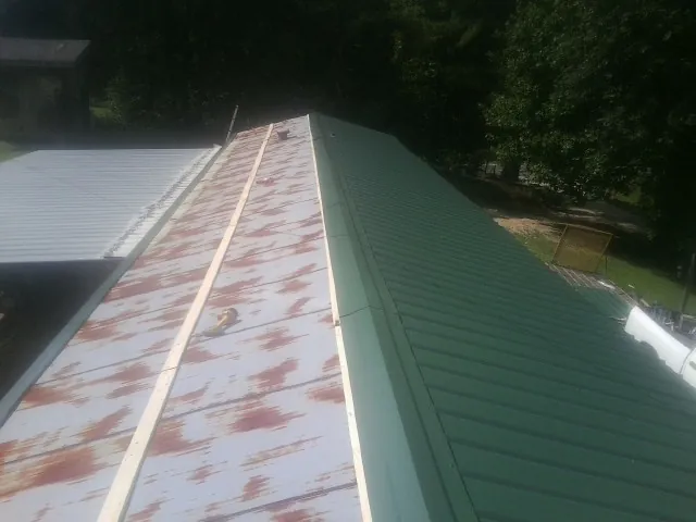 Old rusted panels beside newly installed green metal roofing in Owensville