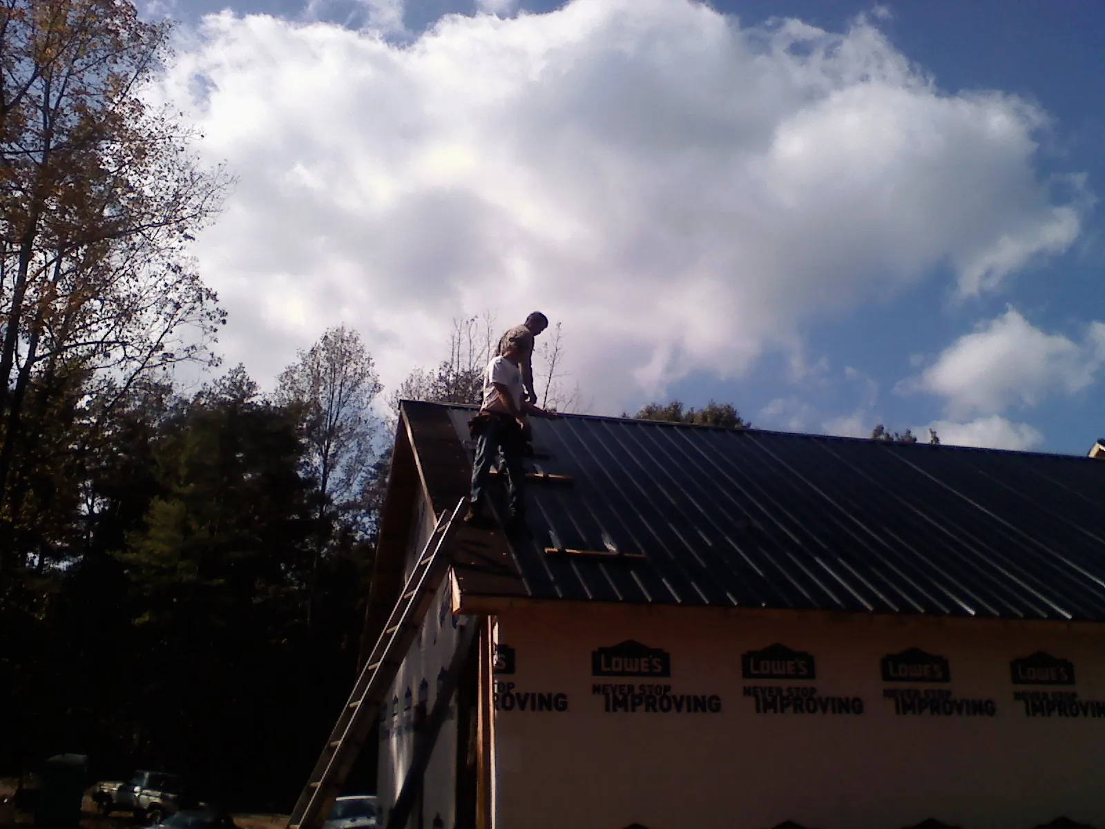 Roofer fastening dark metal panels high against a cloudy sky, from a Roof Inspection job in Owensville