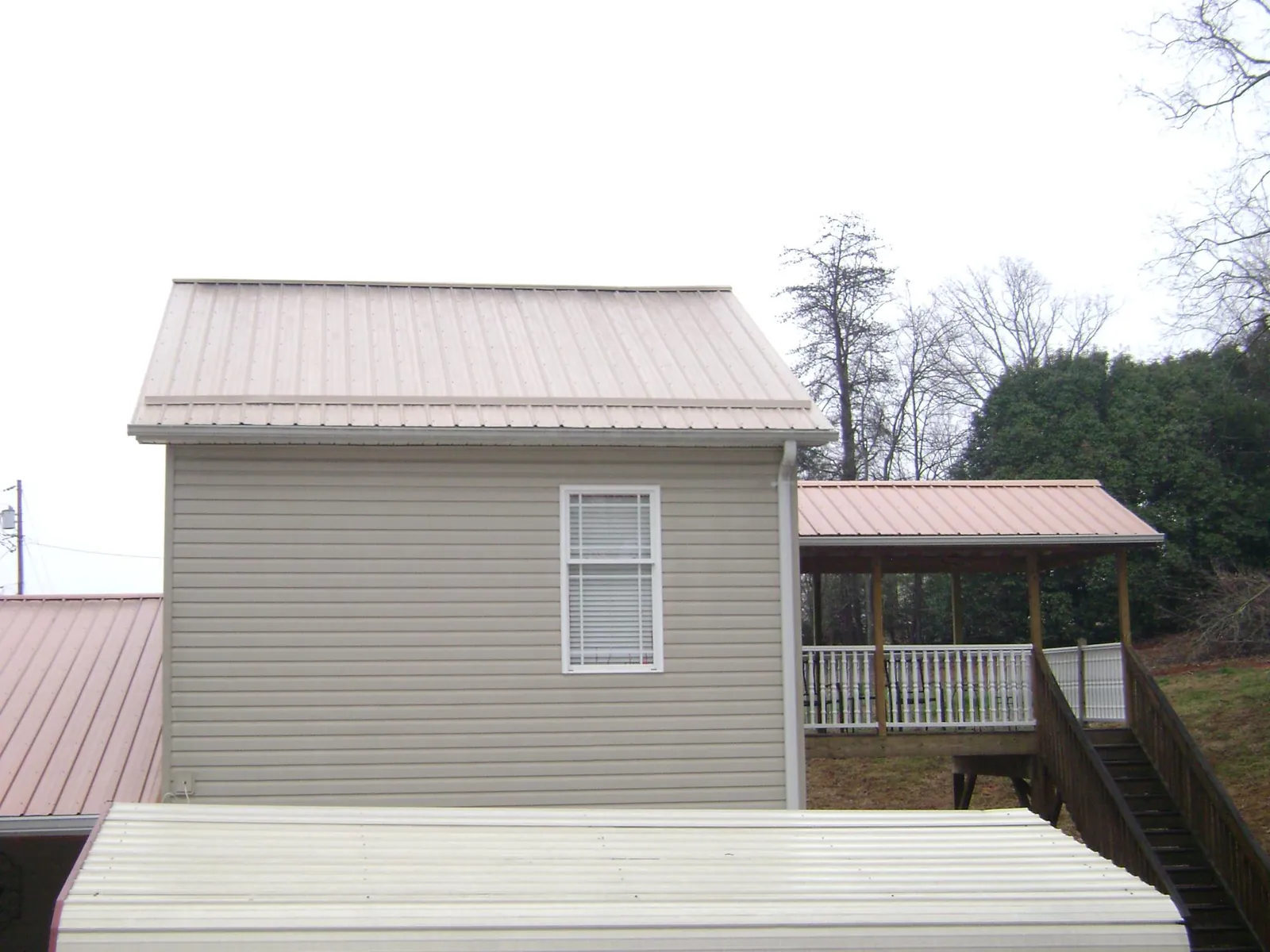 Tan metal roofs on a two story addition and attached porch, from a Roof Replacement job in Owensville